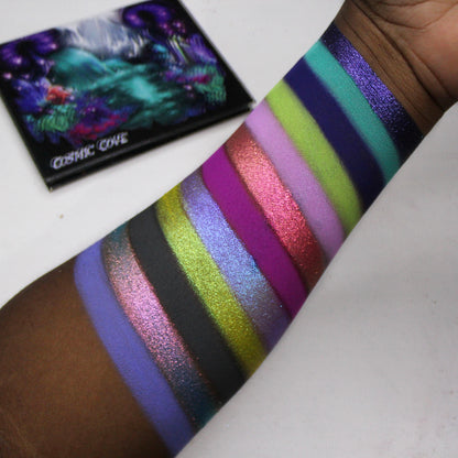 Cosmic Cove swatches on deep skin tone showing all twelve shades, with the closed palette in the corner showing the painted cover artwork