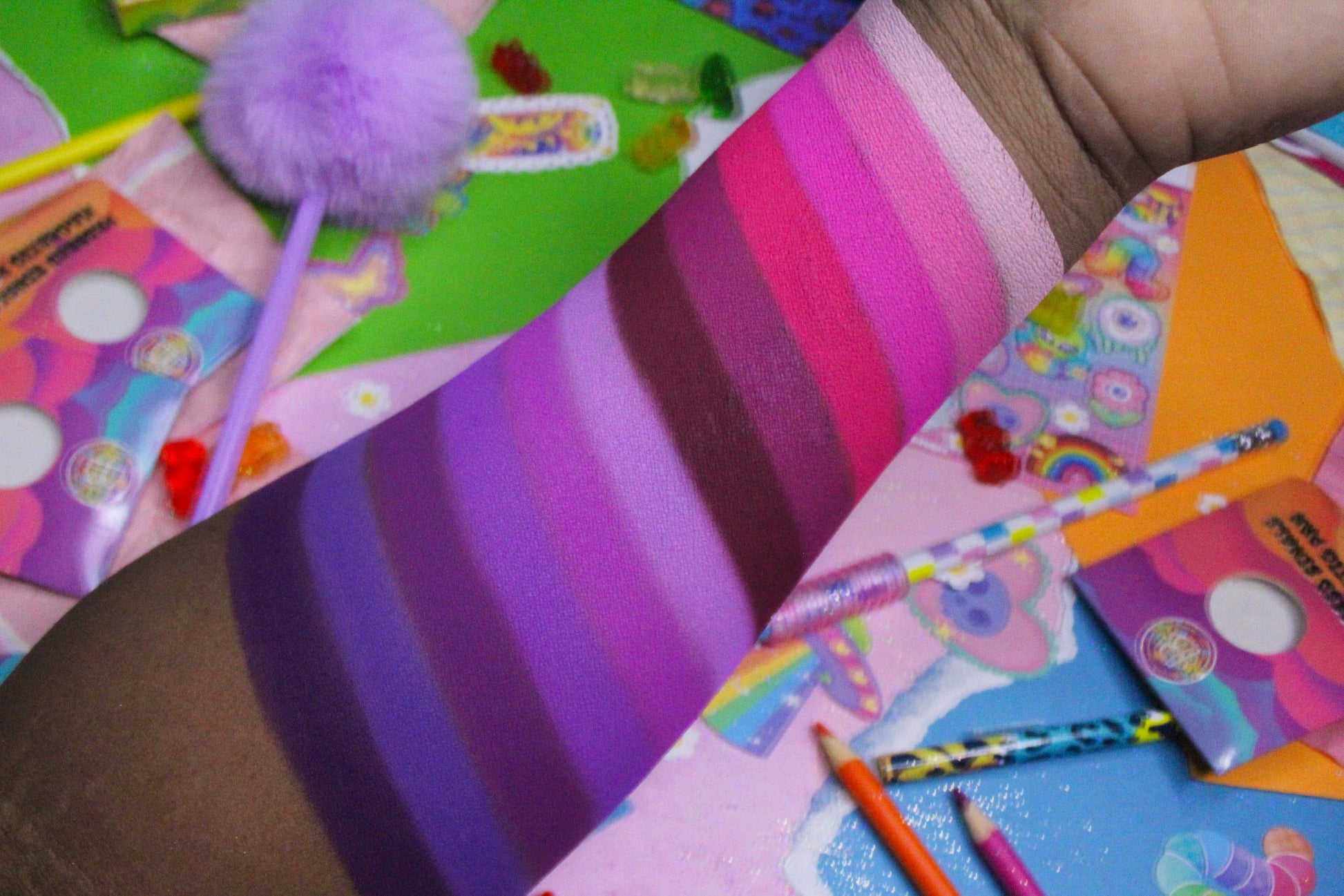 Close-up of pink to purple stripe swatches on deep skin over a colourful 90s sticker collage