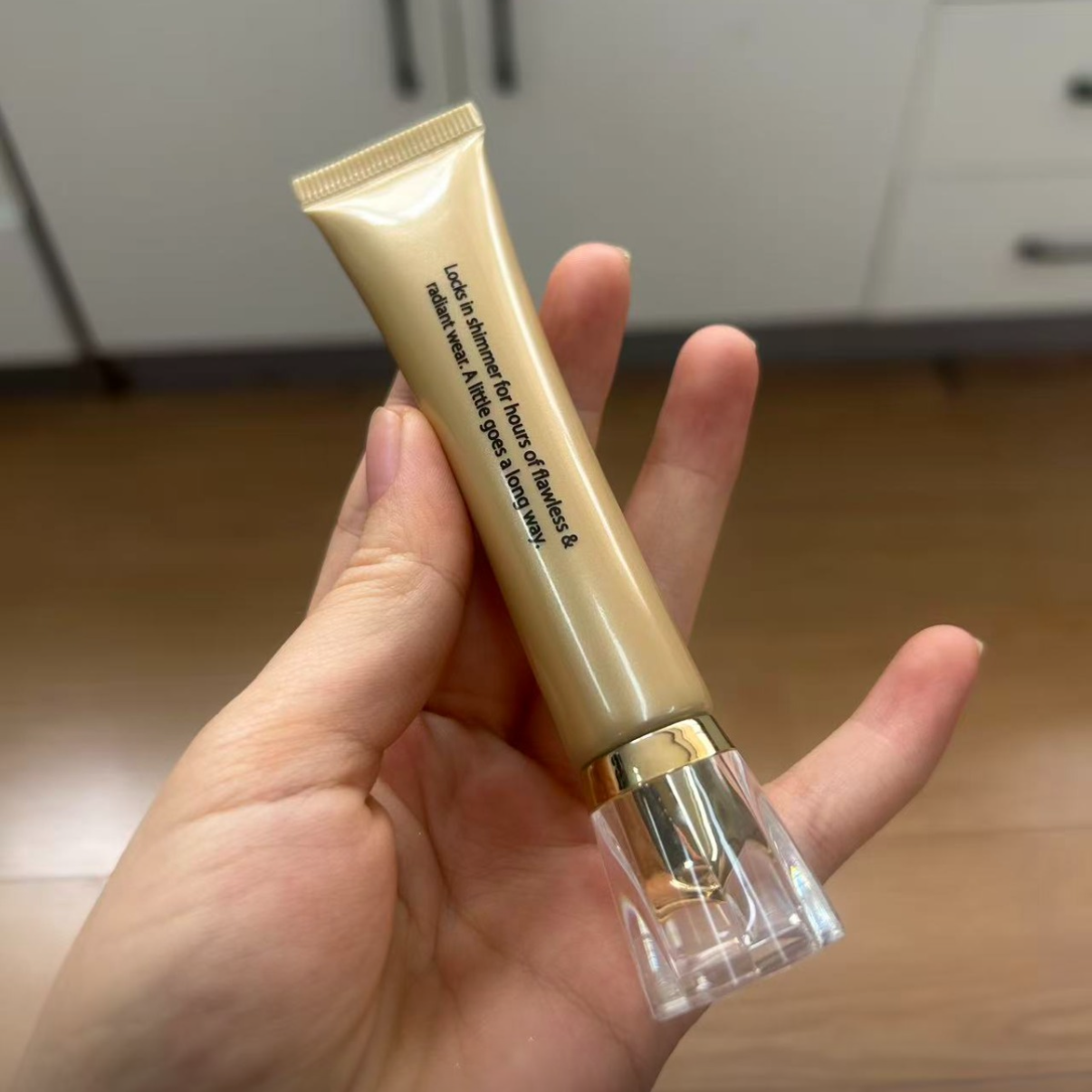 Back of the gold Lock in Glow shimmer base tube held in hand, showing the product description text