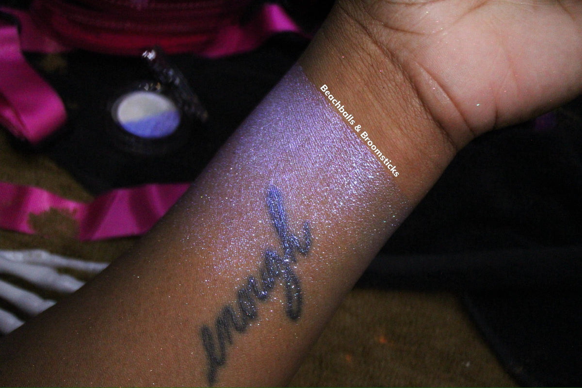 Beachballs and Broomsticks swatched along a forearm on deep skin, shot on pink satin beside the compact.