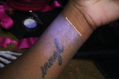 Beachballs and Broomsticks swatched along a forearm on deep skin, shot on pink satin beside the compact.