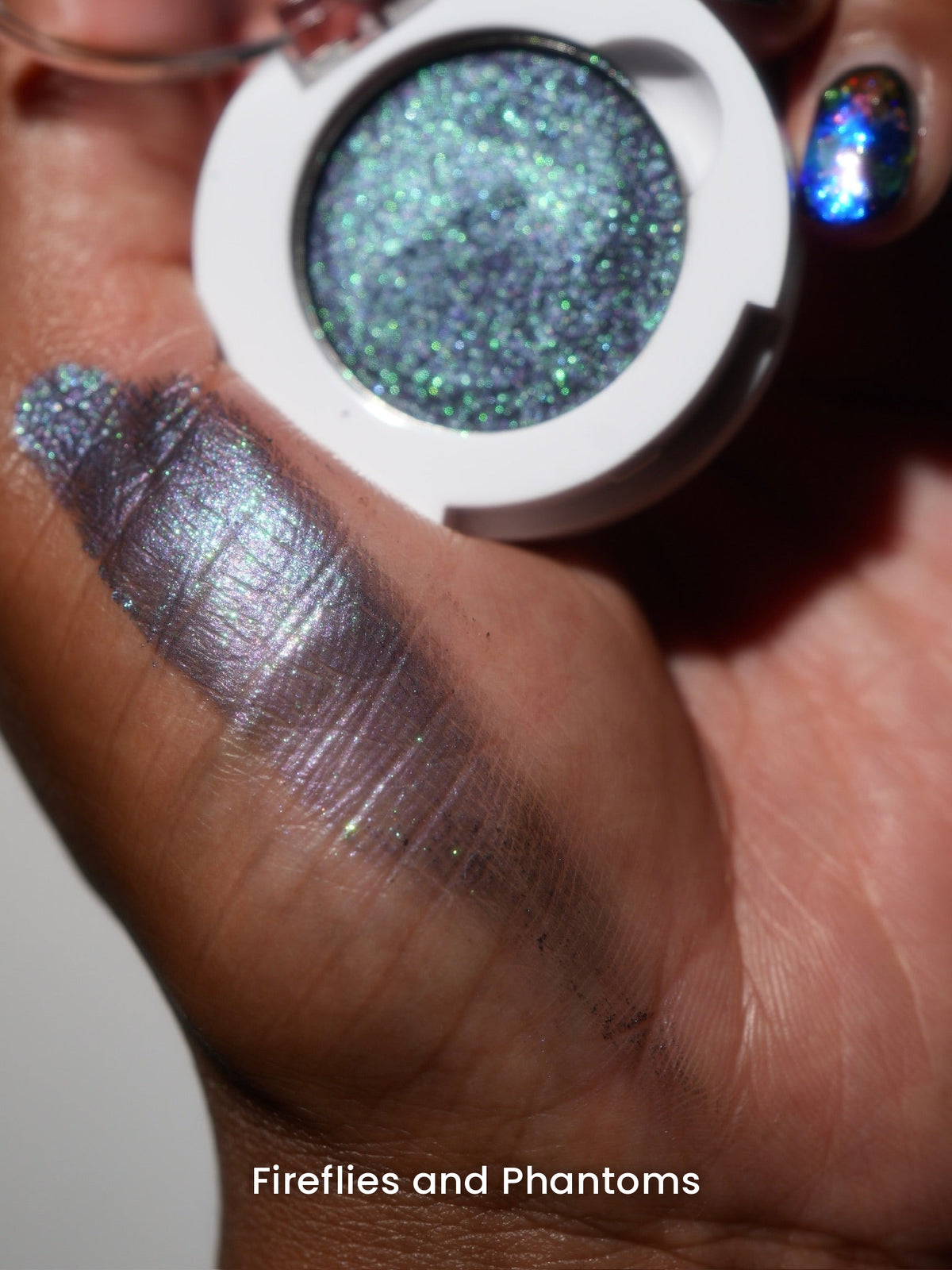 Fireflies and Phantoms compact in hand with a finger swatch on deep skin