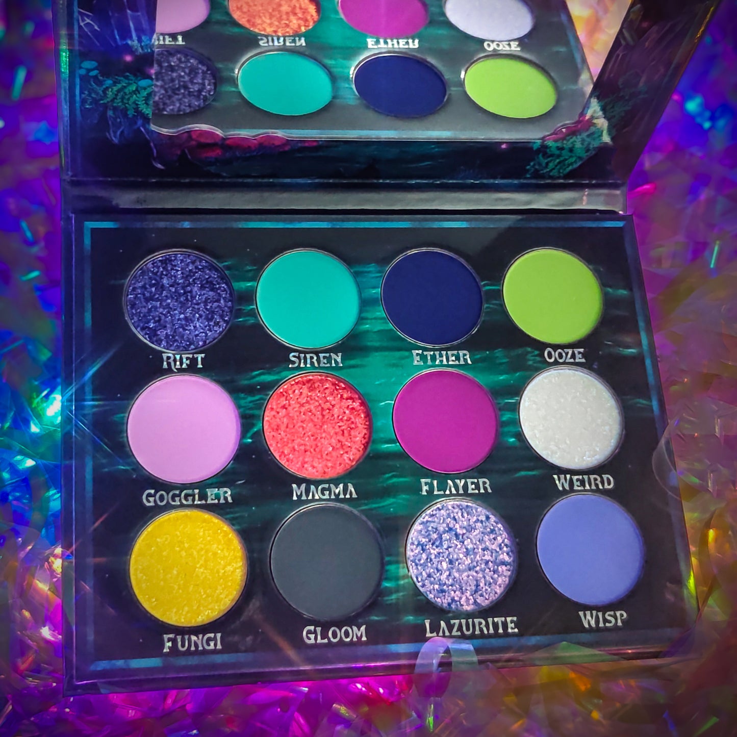 Cosmic Cove palette open from above on an iridescent background, twelve pans in three rows with shade names visible: Rift, Siren, Ether, Ooze across the top