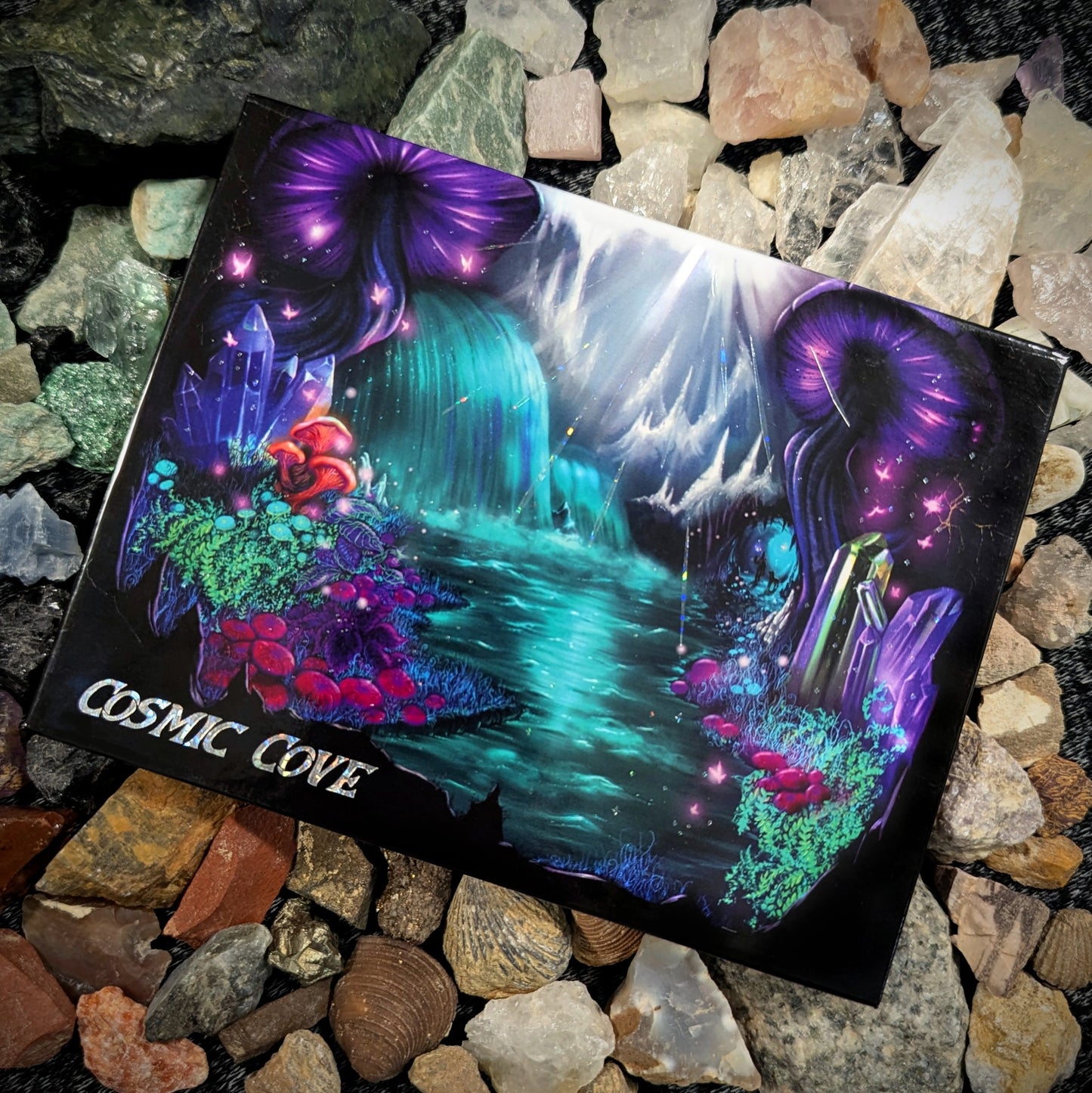 Cosmic Cove closed palette on a bed of multicoloured rocks and crystals, cover art shows purple jellyfish, teal waterfall, mushrooms, and coral