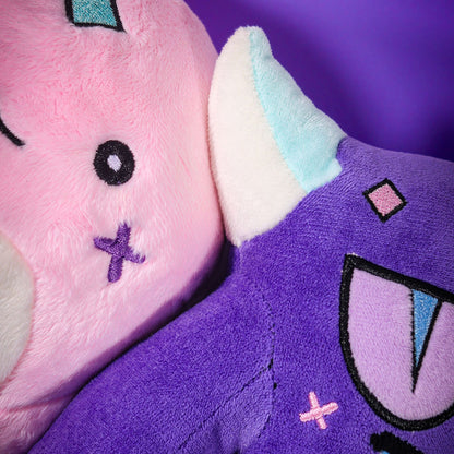 Close-up of the Gleam and Gloom plush faces side by side, showing the embroidered stitch details.