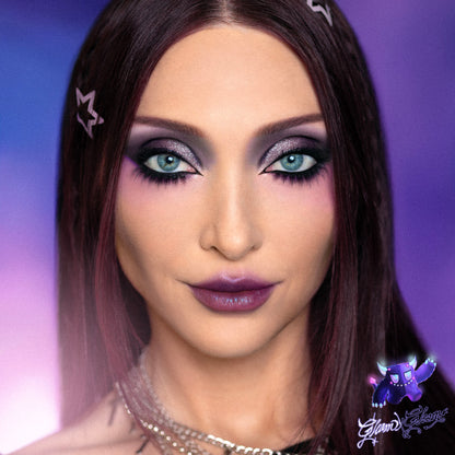 Model wearing a Gloom eye look, deep purple and teal smoke around the eye with a dark plum lip.