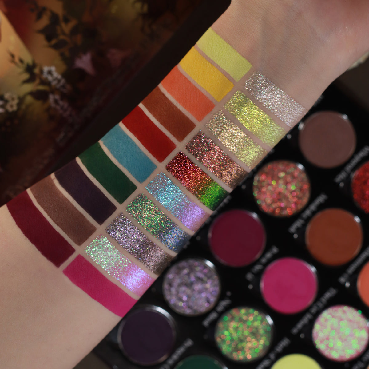 Close-up arm swatches of the mattes and shimmers on light skin, beside the open pans.
