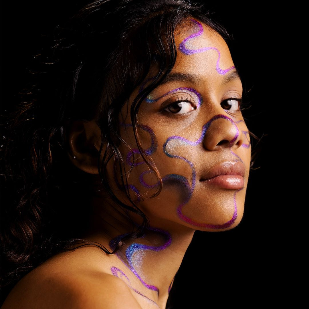 Side-profile portrait on black, with iridescent purple and blue swirling line art painted across the cheek, temple, neck and shoulder.