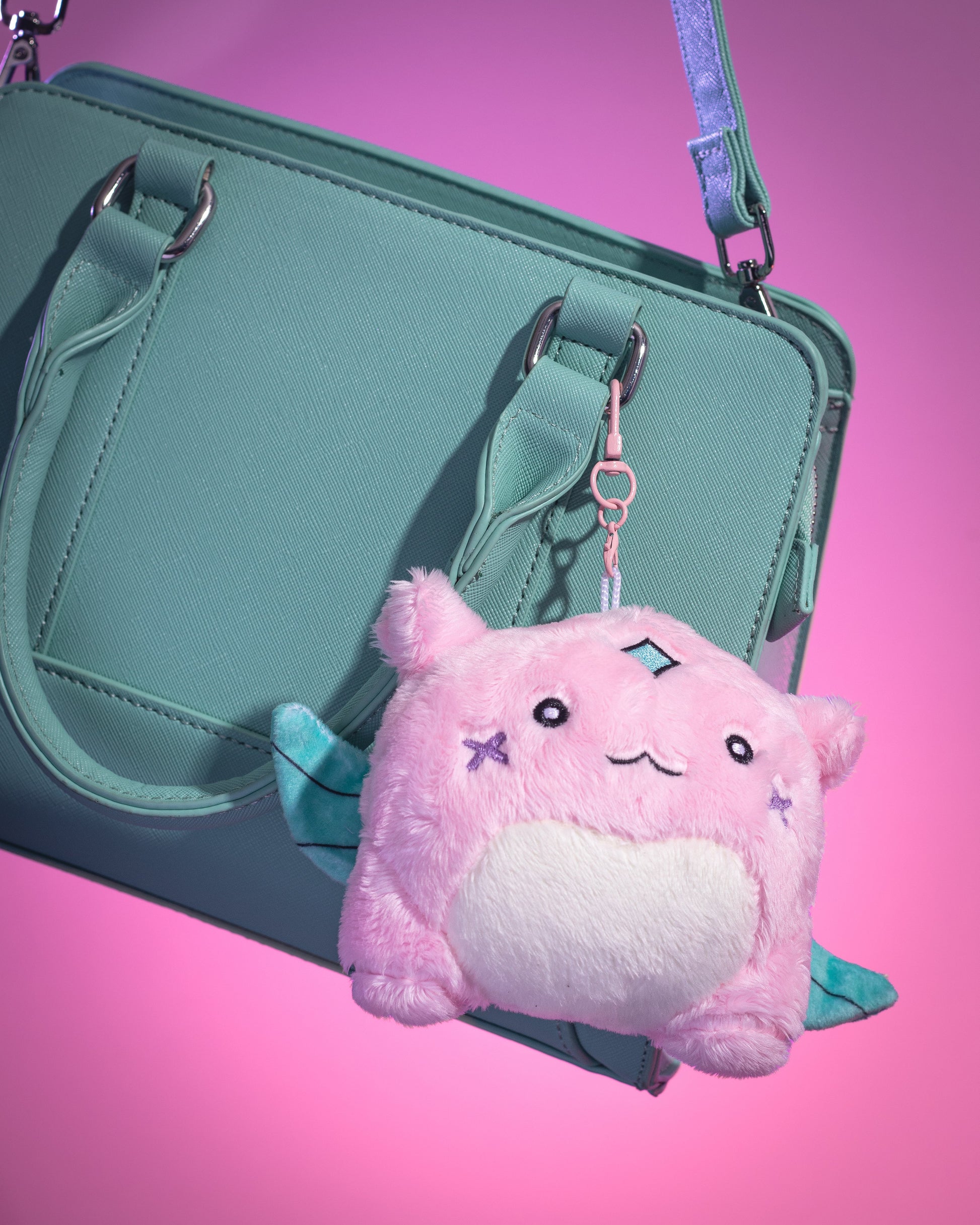 Gleam plush keychain clipped to the handle of a teal handbag against a pink backdrop.