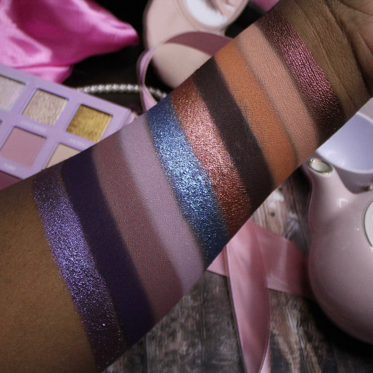 Arm swatches of Dollhouse shades on deep skin: purples, mauves, blue and copper shimmers