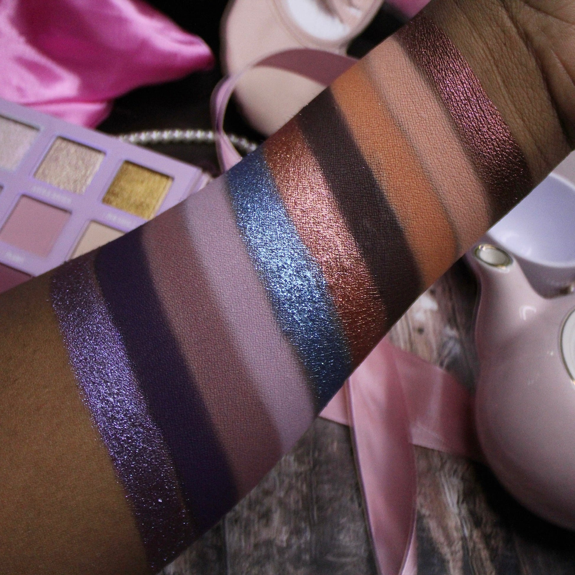 Arm swatches of Dollhouse shades on deep skin: purples, mauves, blue and copper shimmers