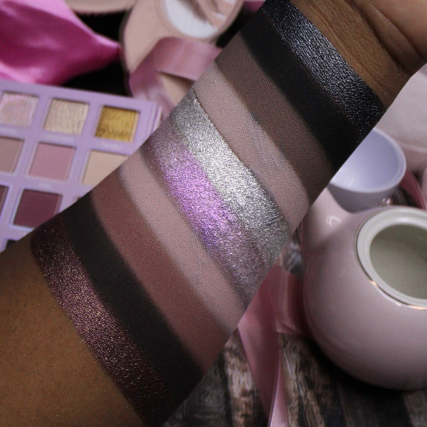 Arm swatches of Dollhouse shades on deep skin: taupes, silver and purple shimmers, deep browns