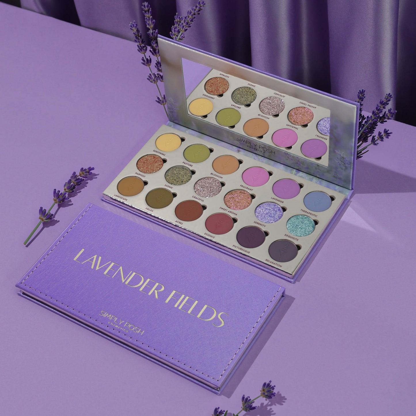 Simply Posh Lavender Fields eyeshadow palette open and closed on a lavender background, lilac faux-leather cover with gold lettering and 18 pans inside