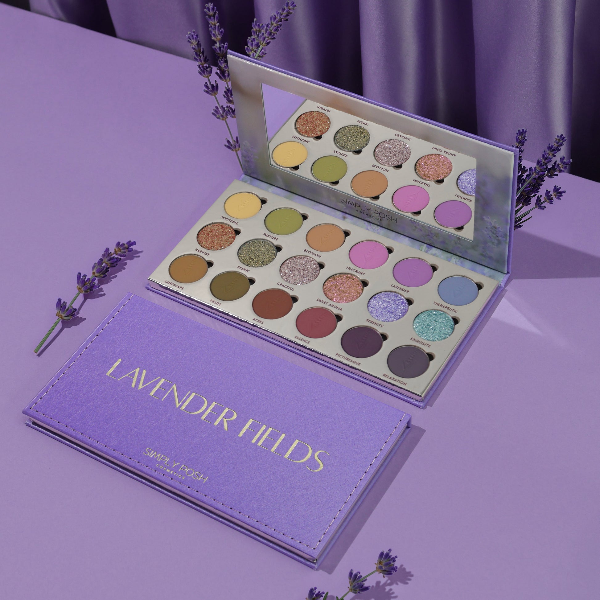 Simply Posh Lavender Fields eyeshadow palette open and closed on a lavender background, lilac faux-leather cover with gold lettering and 18 pans inside