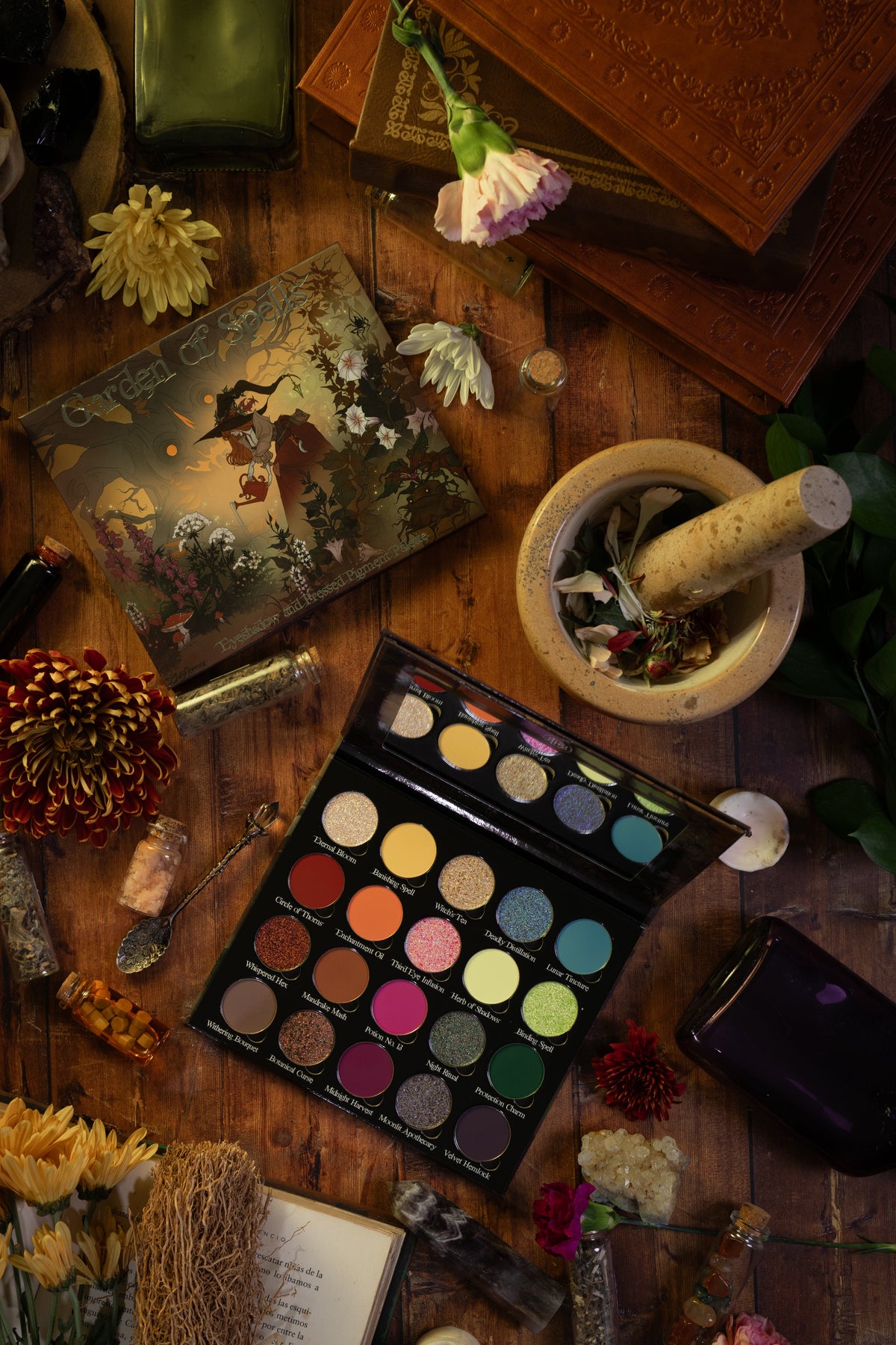 Garden of Spells palette open on a wooden table with its cover, a mortar and pestle and dried flowers.