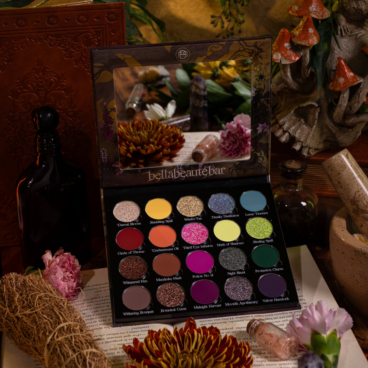 Garden of Spells palette open on a spellbook, 20 named pans under a mirrored lid, among dried flowers, a herb bundle and clay mushrooms.