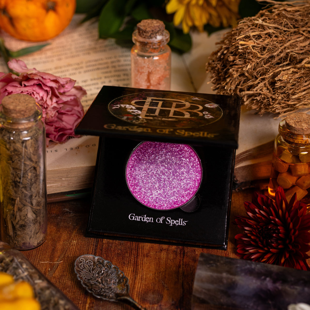 Garden of Spells highlighter compact open among dried flowers, herb jars and a small pumpkin.