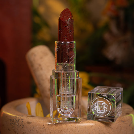 Garden of Spells sparkle balm in its clear tube, standing in a stone mortar beside the monogram cap.
