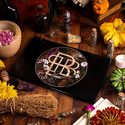 The closed Garden of Singles palette with its gold monogram and botanical lid art, on a witch's table with pumpkins, herbs and crystals
