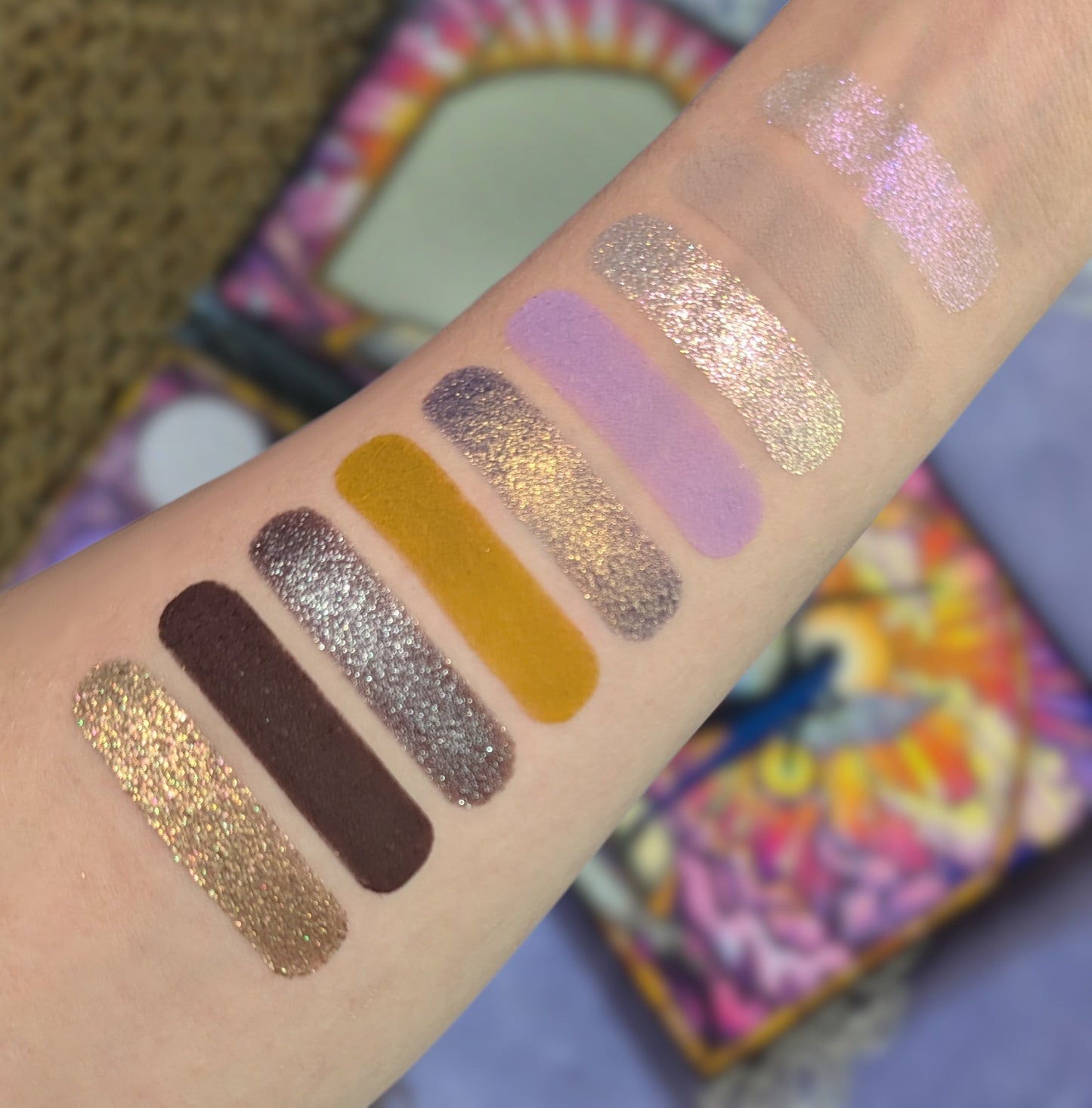 Paladin swatches on a light skin tone arm, nine stripes running gold sparkle, deep brown, silver purple, mustard, lilac and pale taupe, palette blurred behind