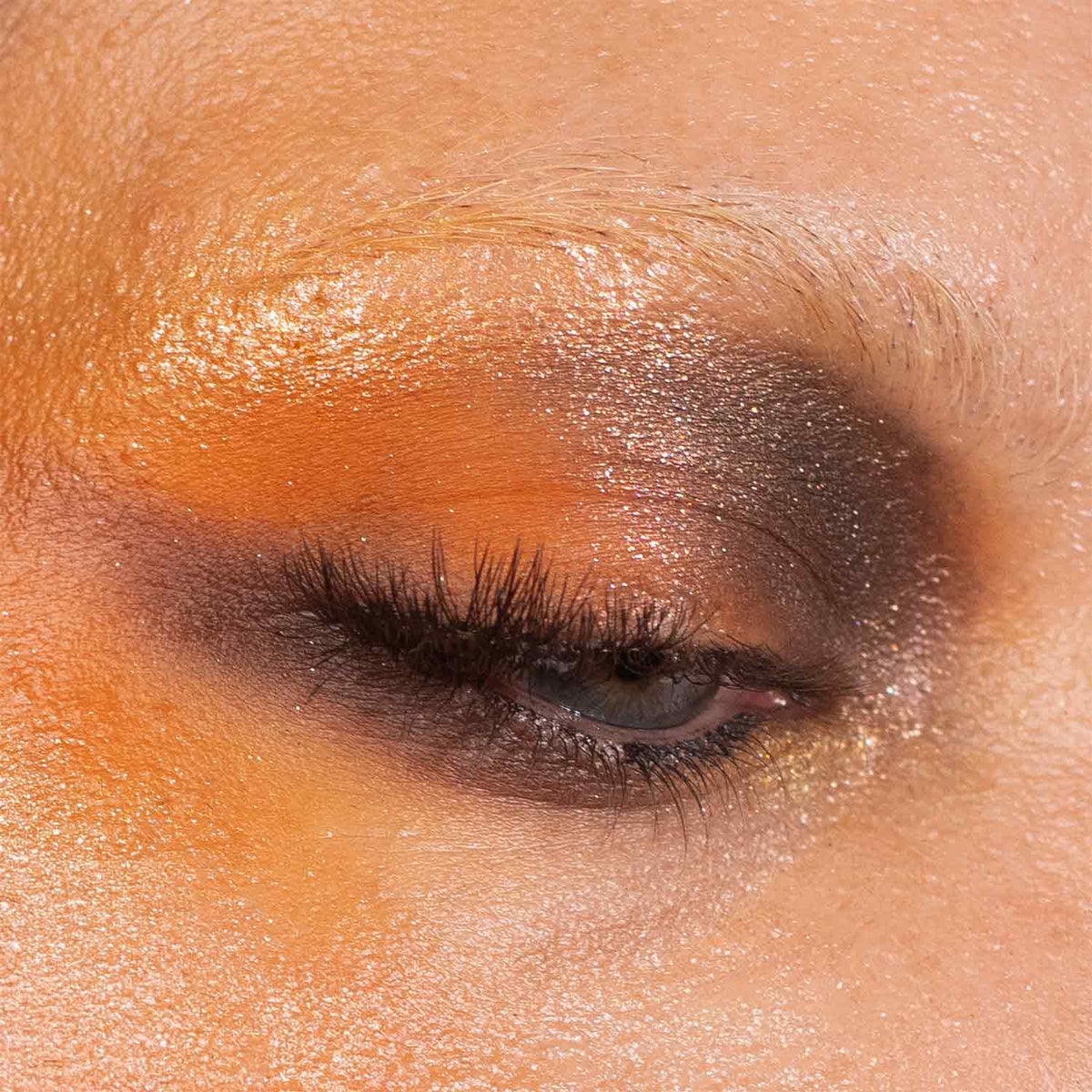 Close-up of a warm orange and brown eye look with a gold sparkle lid