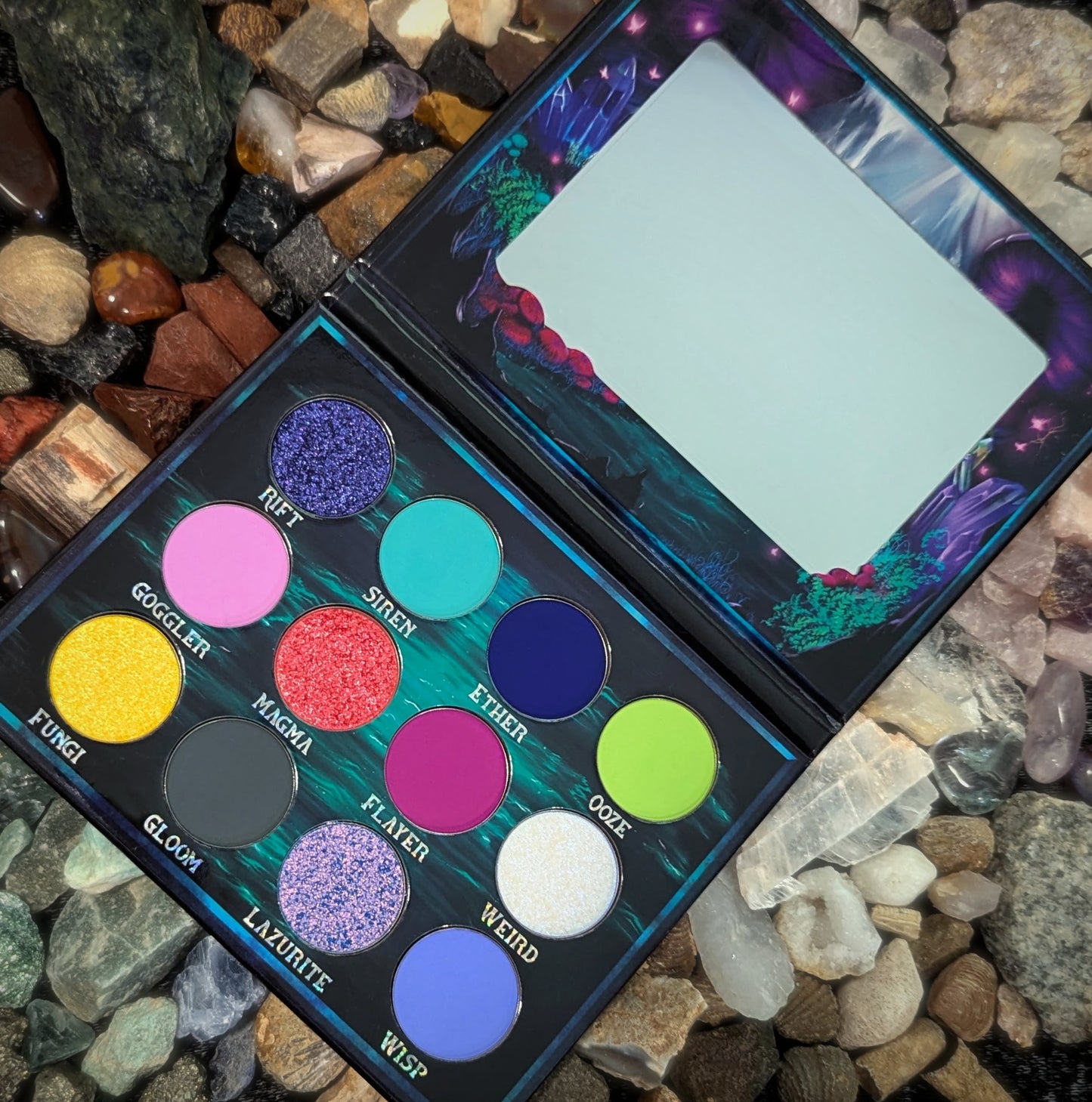 Cosmic Cove palette open outdoors on a bed of natural rocks and crystals, all twelve pans labelled with shade names visible