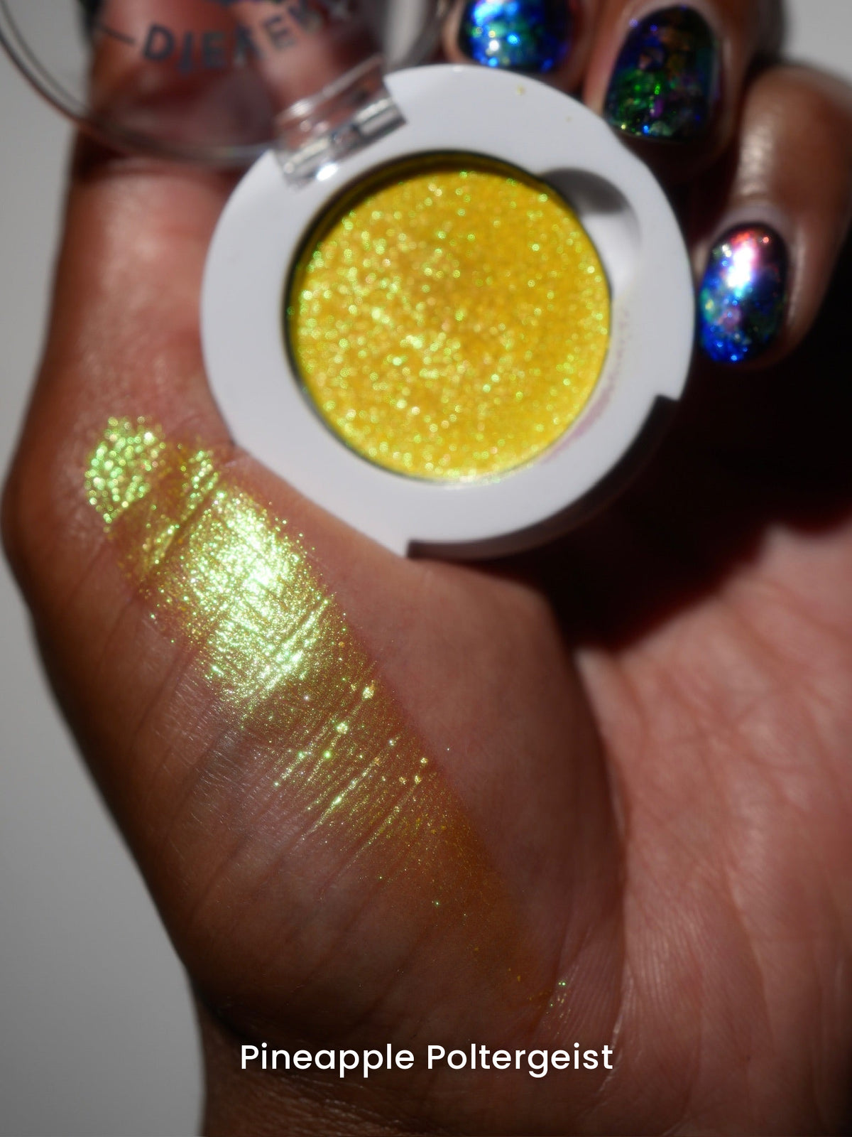 Pineapple Poltergeist compact in hand with a finger swatch on deep skin