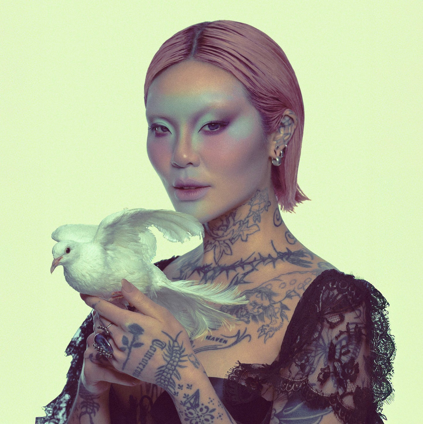 Model with a green-toned Fauna look holding a white dove, wearing lace