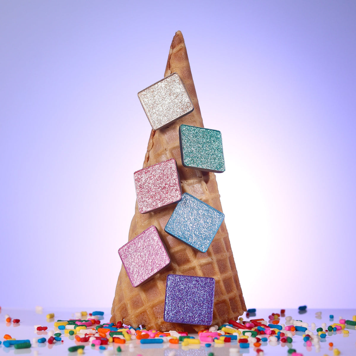 The six Sickly Sweet shimmer pans stacked against a waffle cone with rainbow sprinkles
