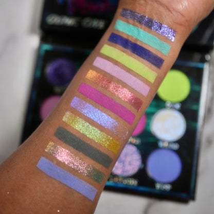 Cosmic Cove swatches on medium skin tone showing all twelve shades in stripes, the open palette visible in the background