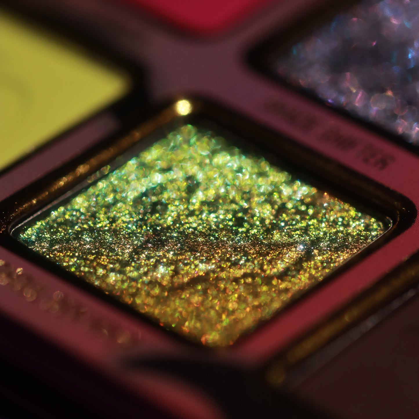 Macro close-up of a green and gold colour-shifting sparkle shade in its gold-framed pan