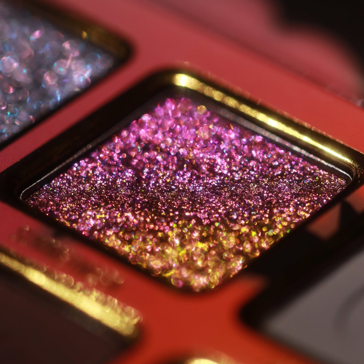 Macro close-up of a pink-to-gold colour-shifting sparkle shade in its gold-framed pan