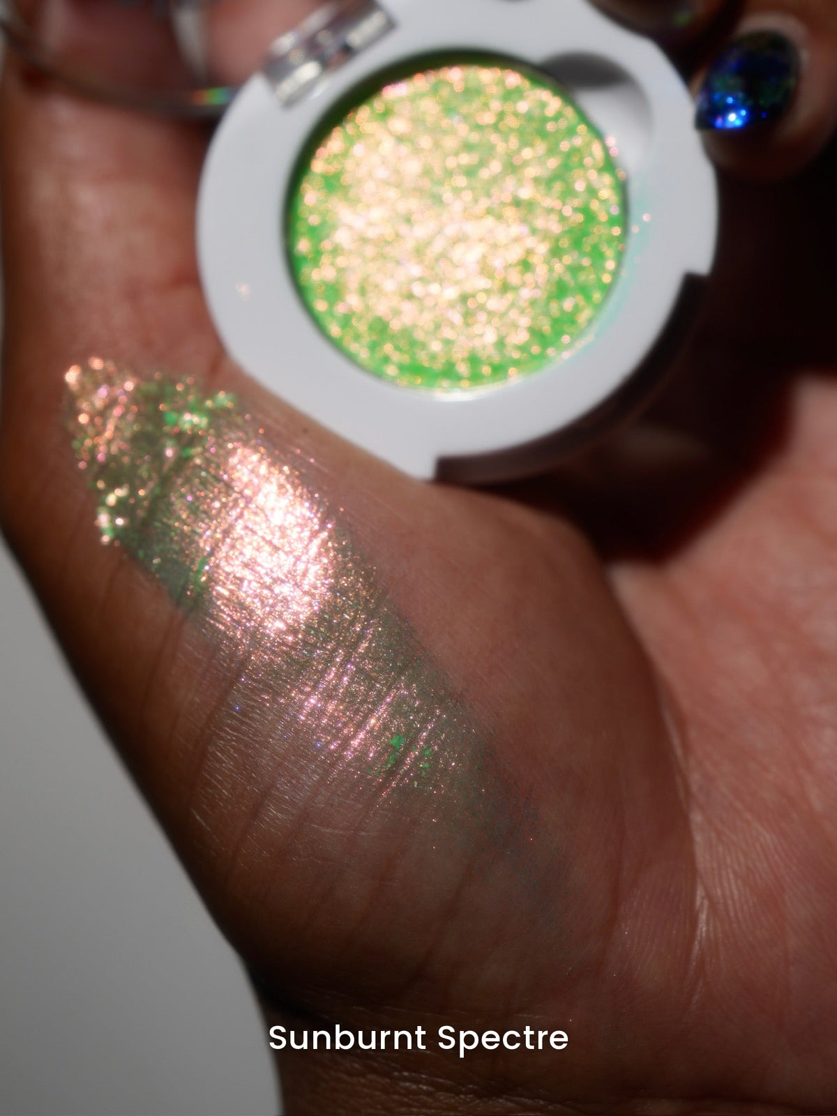Sunburnt Spectre compact in hand with a finger swatch on deep skin