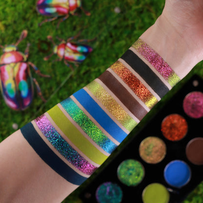 Arm swatches of all ten shades on a fair wrist next to the open palette, set on a mossy green ground with two scarab beetle figures.