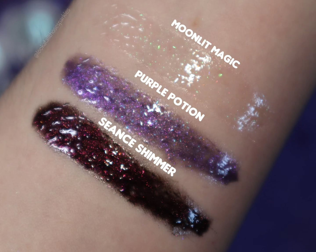 Arm swatches of the three glosses on fair skin, labelled Moonlit Magic, Purple Potion and Seance Shimmer