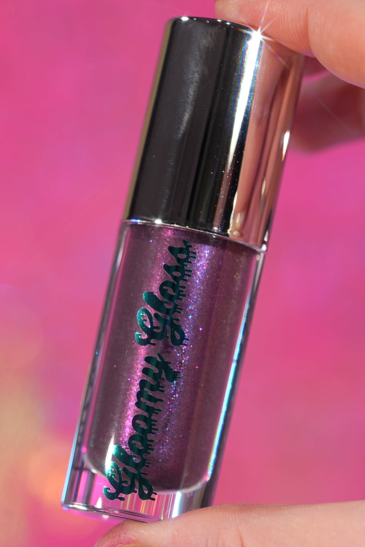 Purple Potion tube held up against a pink backdrop, purple sparkle showing through the glass