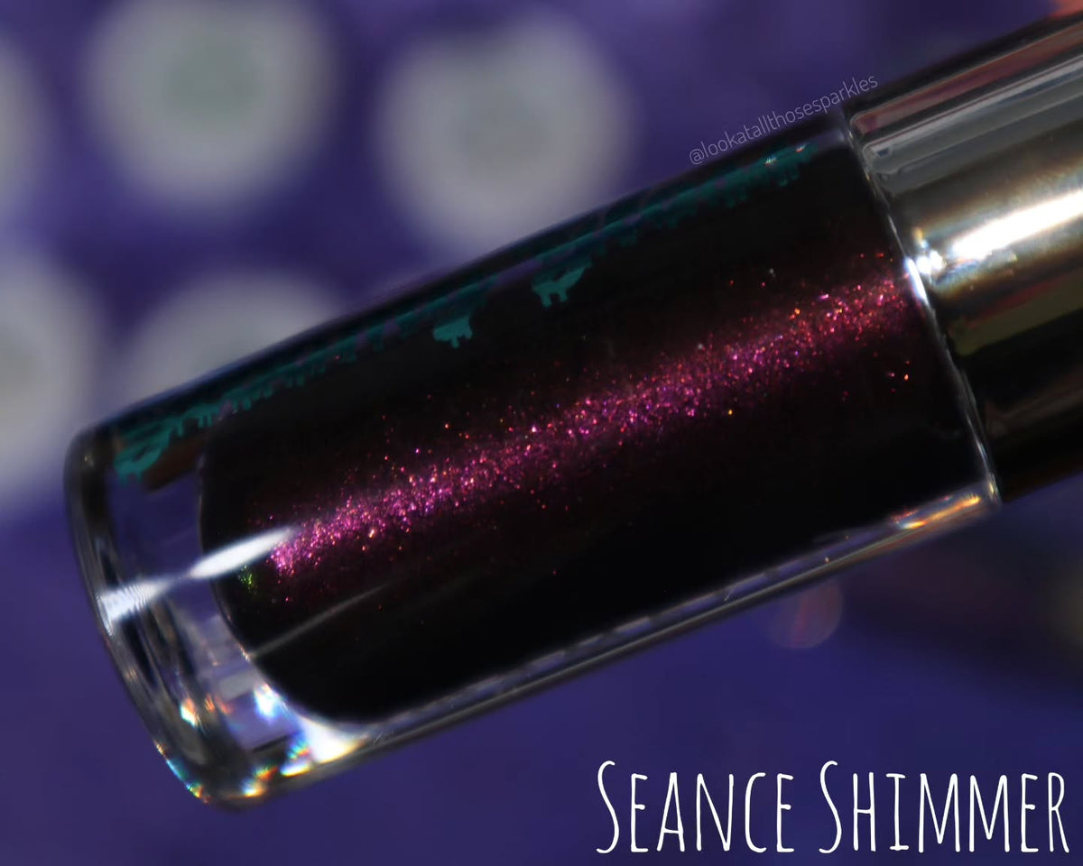 Seance Shimmer tube close-up on a purple backdrop, magenta and gold sparkle in the dark base