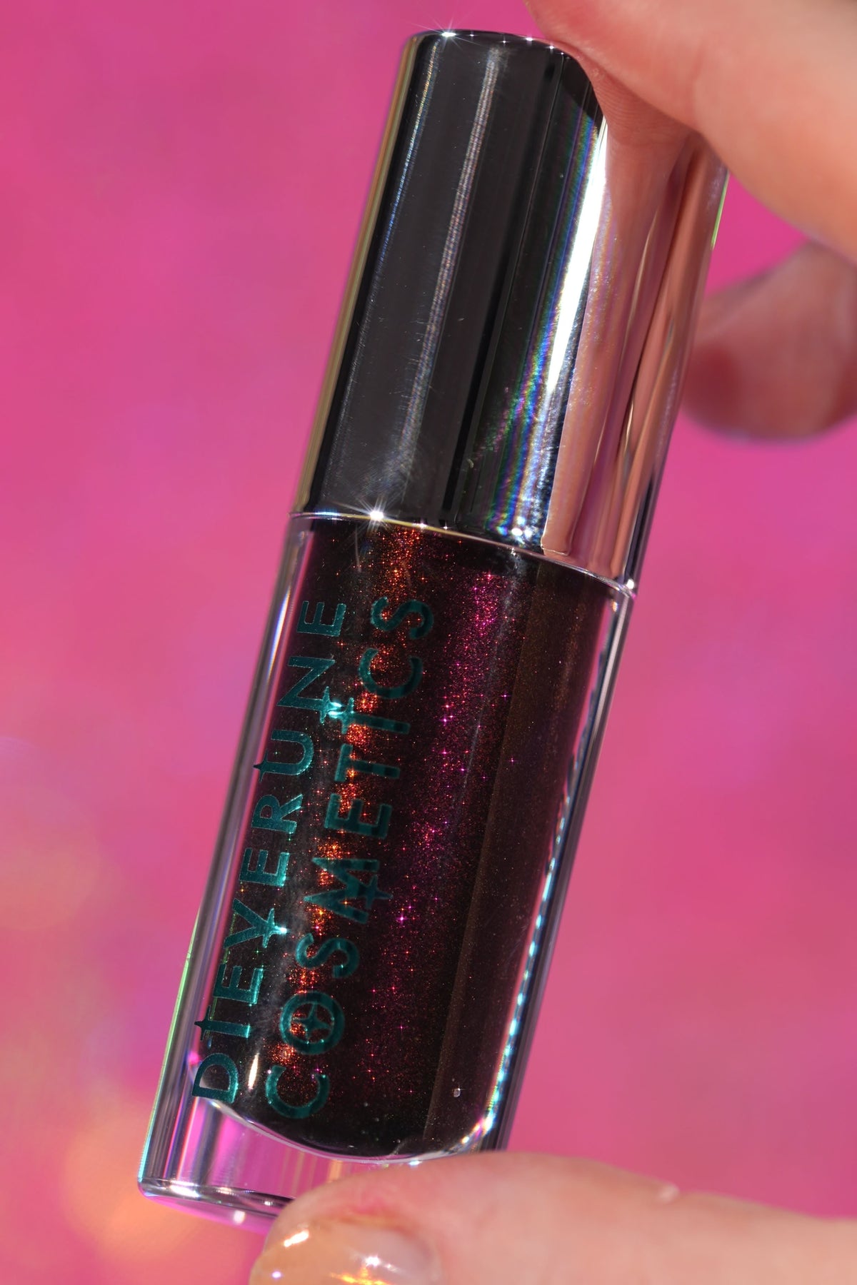 Seance Shimmer tube held against a pink backdrop, showing the dark base and red sparkle