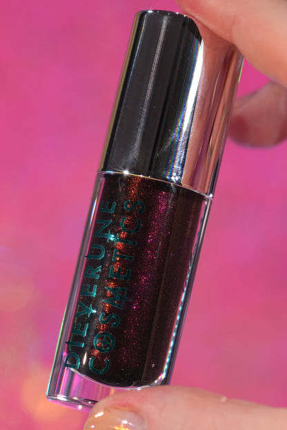 Seance Shimmer tube held against a pink backdrop, showing the dark base and red sparkle