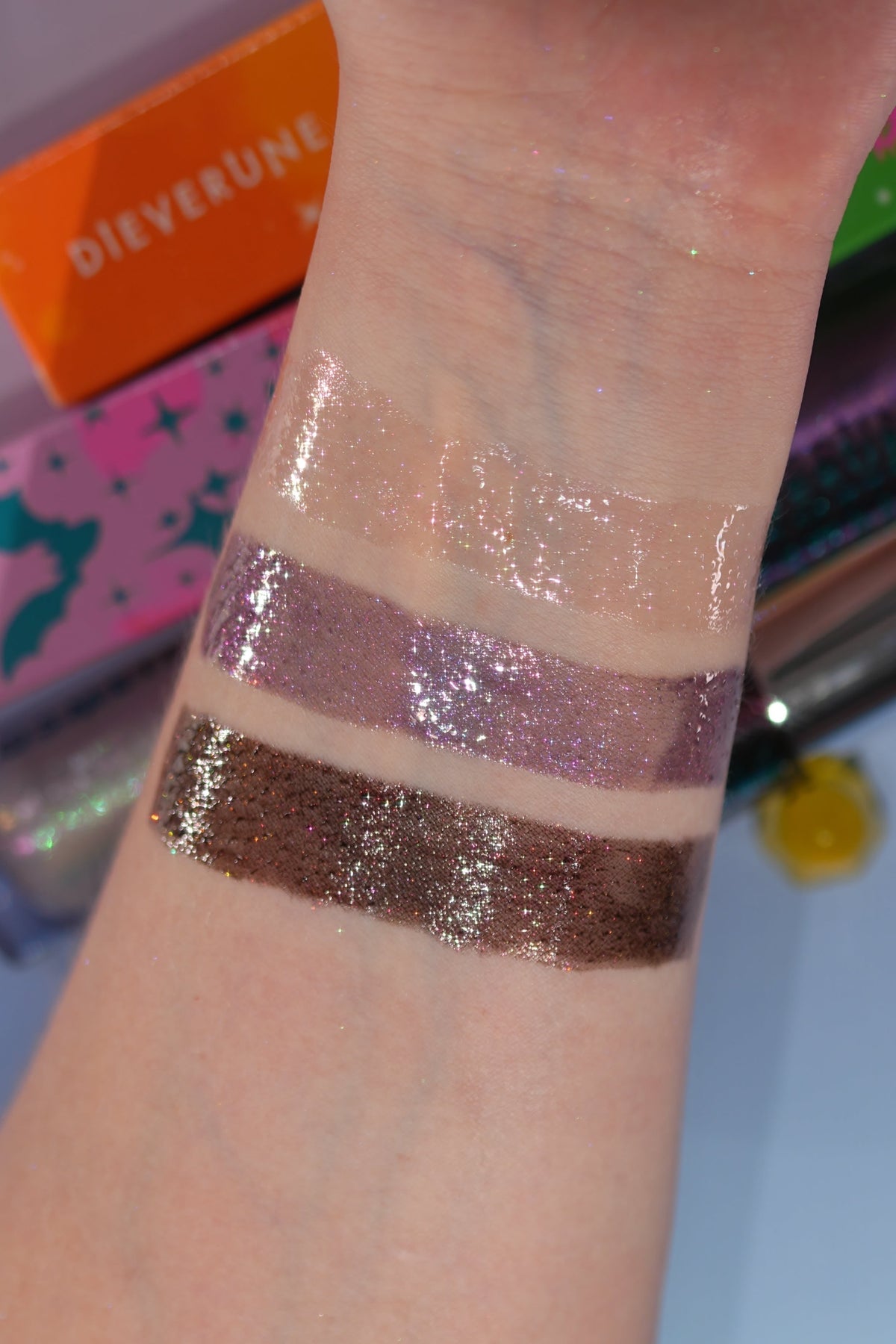Wrist swatches of the three glosses, clear, mauve and deep brown, with Dieverune boxes behind