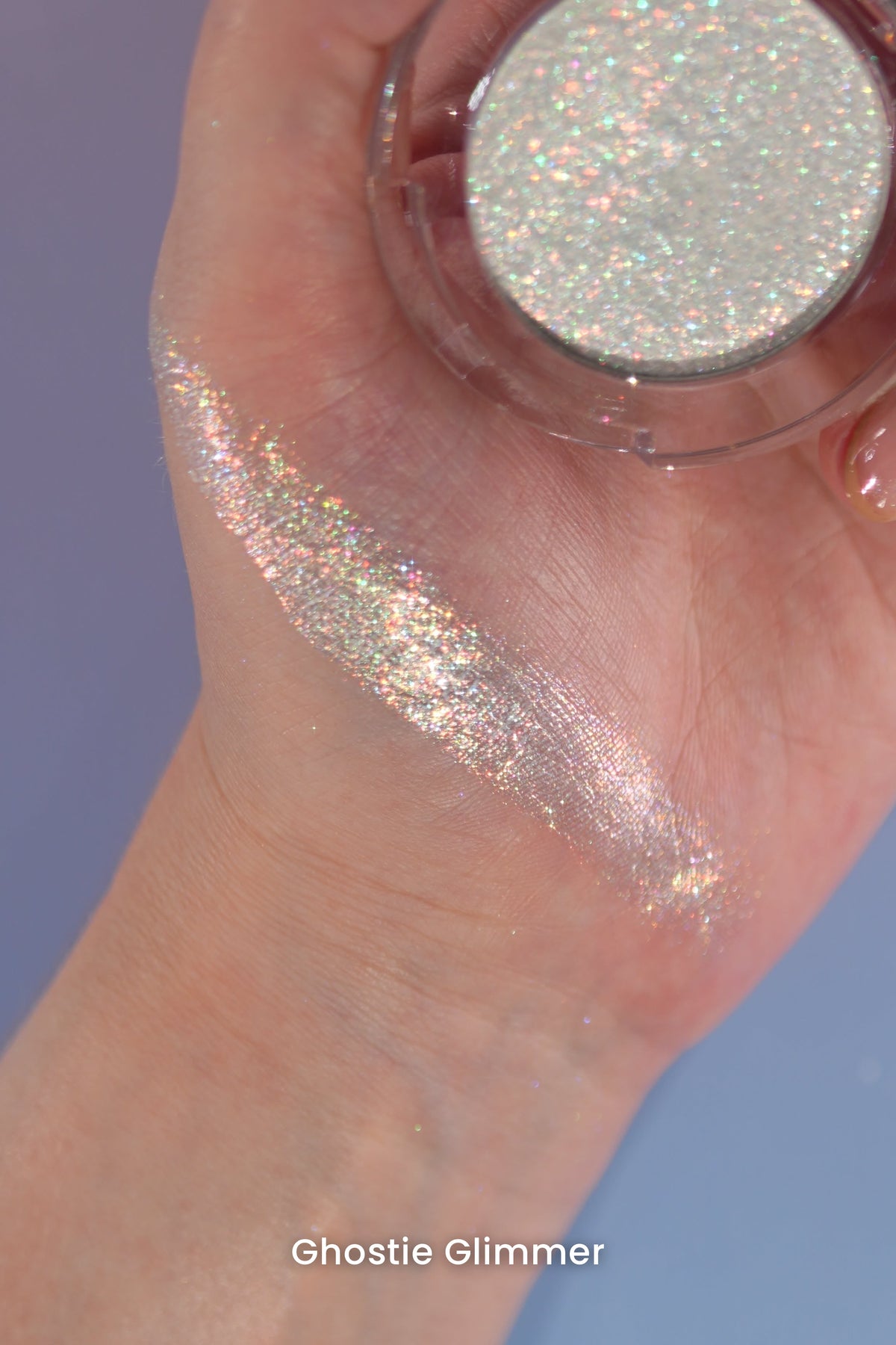Ghostie Glimmer swatch across the palm and wrist, open compact held in hand on a blue backdrop