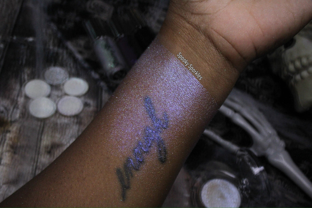 Spooky Sporkle swatch on deep skin, forearm with a tattoo, skull and skeleton hand props, small brand label
