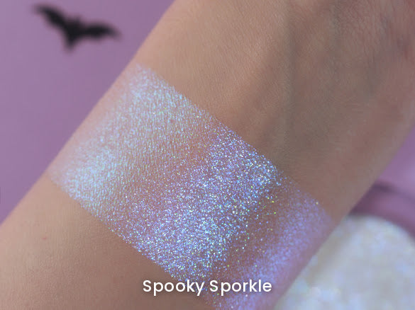 Spooky Sporkle arm swatch on a lilac backdrop with a bat cut-out and the compact behind