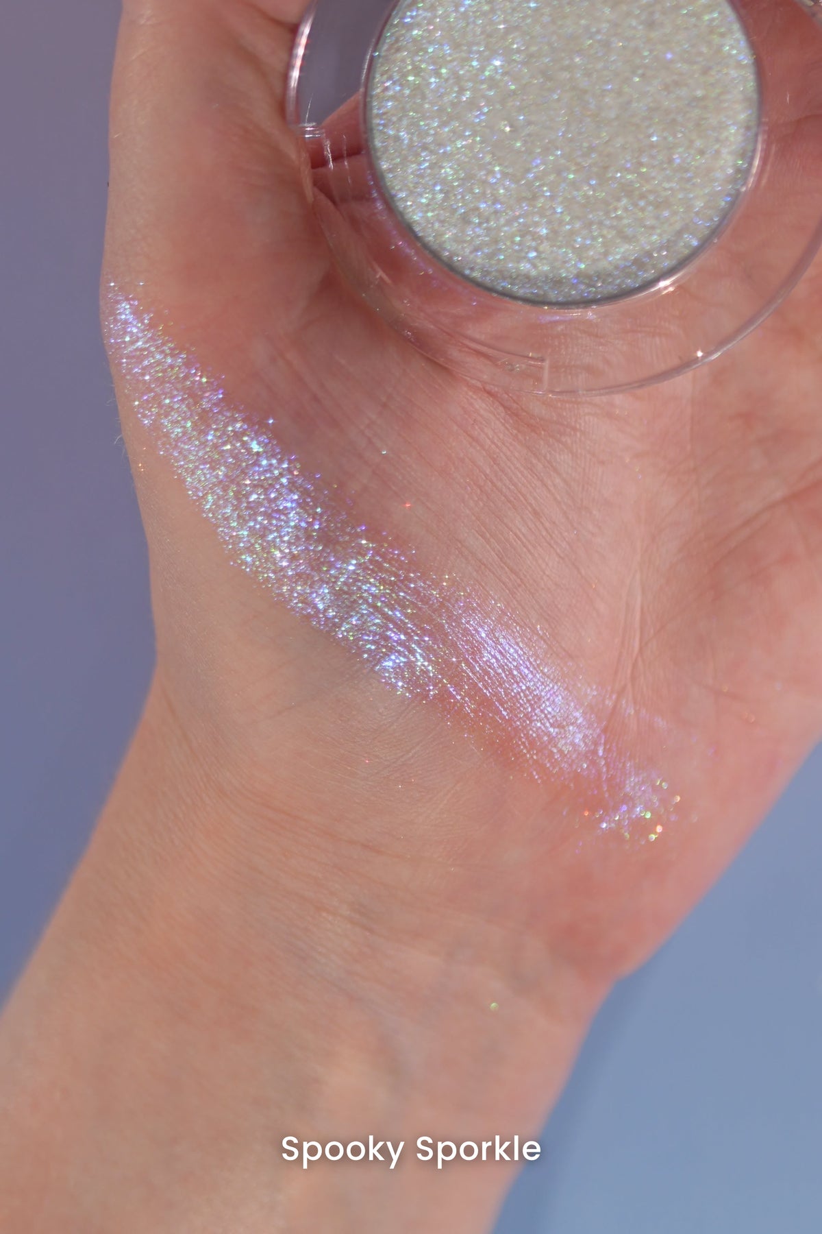 Spooky Sporkle swatch across the palm and wrist, open compact held in hand on a blue backdrop