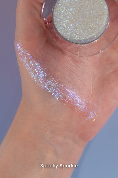 Spooky Sporkle swatch across the palm and wrist, open compact held in hand on a blue backdrop