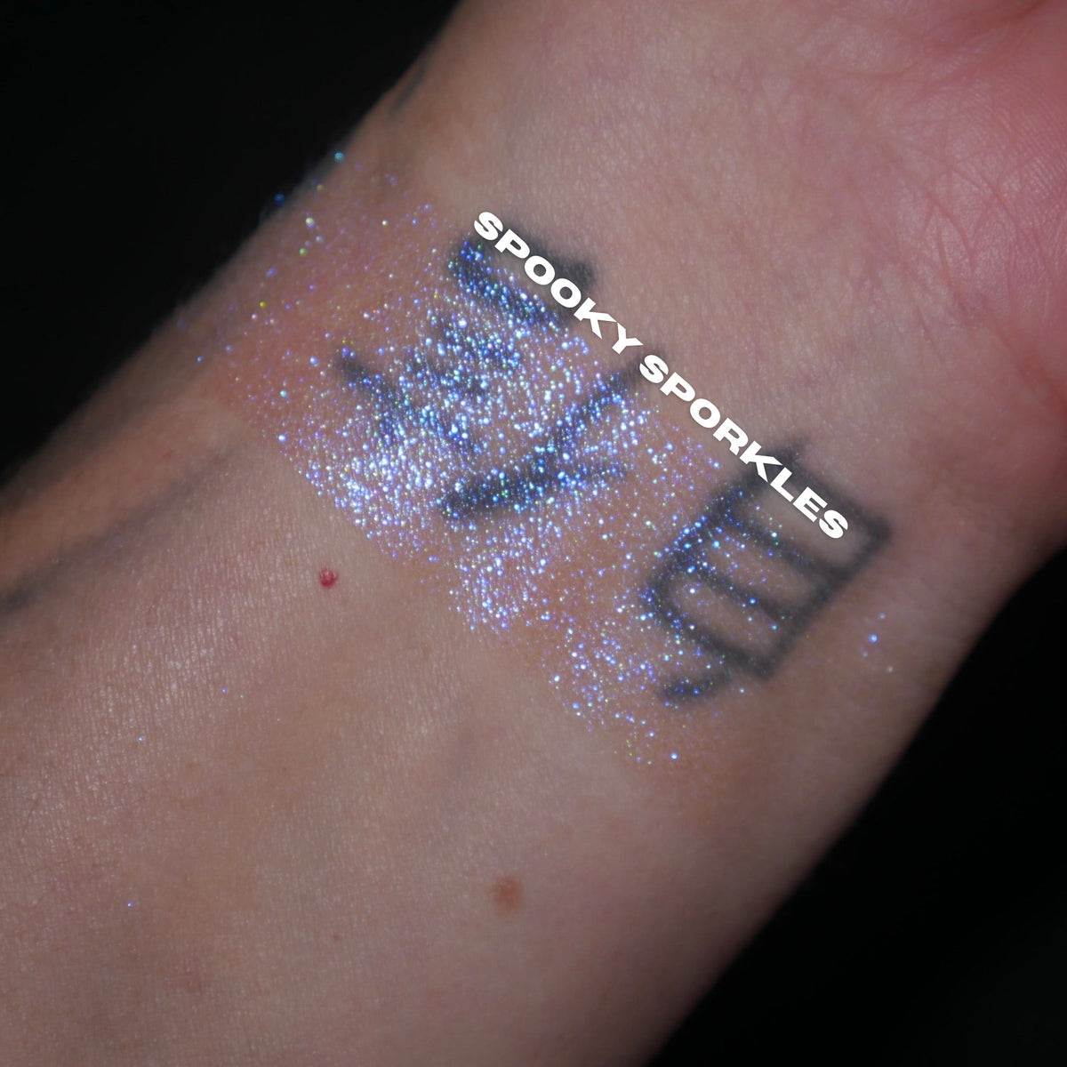 Spooky Sporkle swatch: blue sparkle swatch over a tattooed wrist on a black background, brand label across it