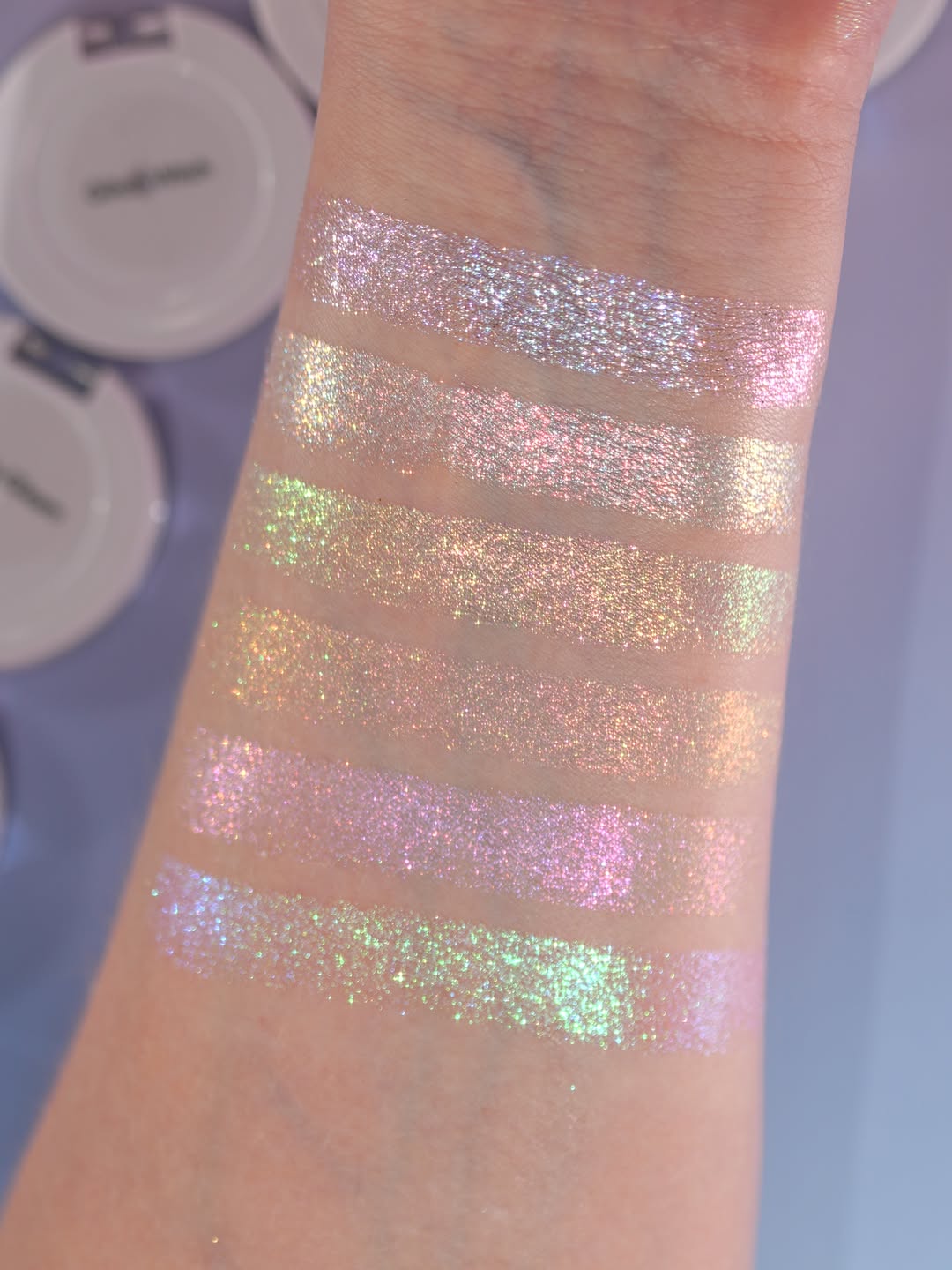 Six Sporkleween singles swatched on light skin in unlabelled stripes, compacts above
