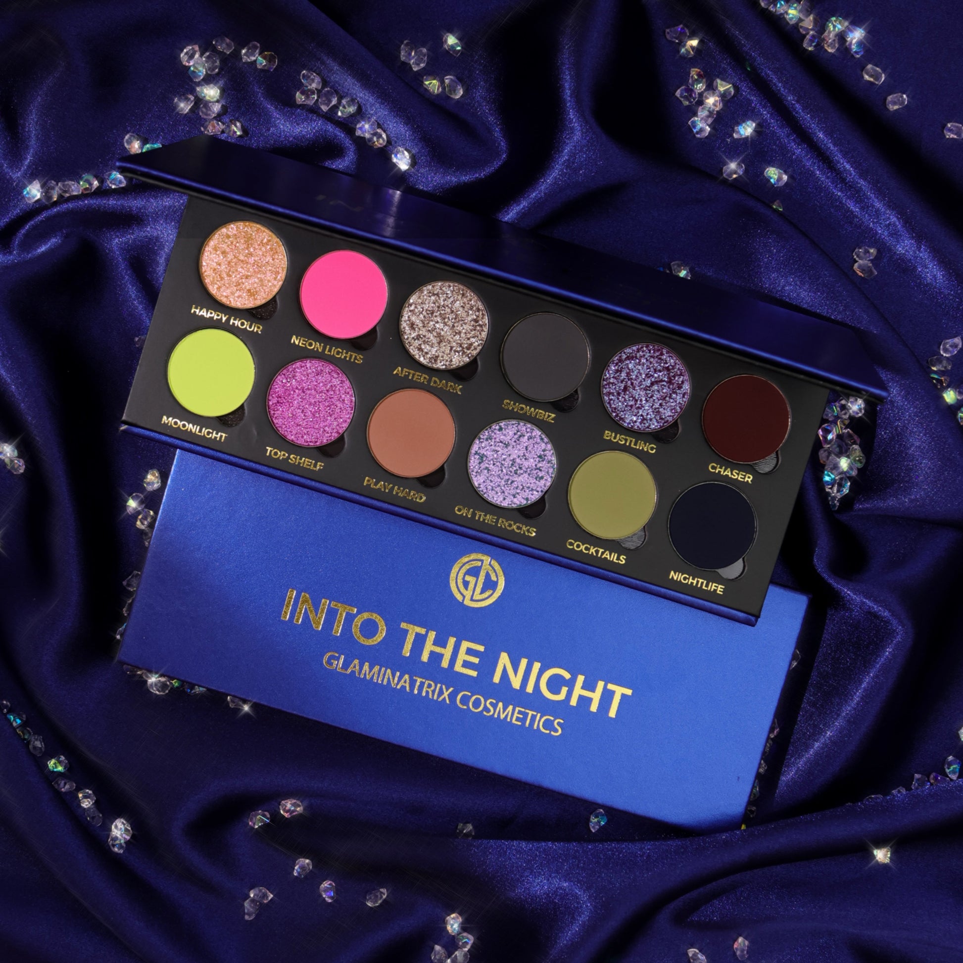Glaminatrix Into the Night eyeshadow palette open on navy satin, 12 shades of neon pink, lime, lilac sparkles, and smoky mattes, with the closed box below