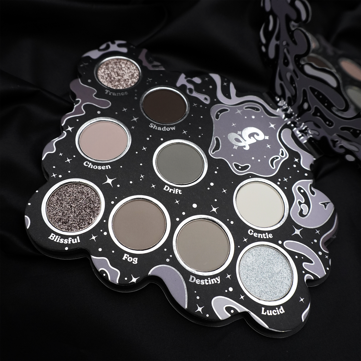 Glisten Cosmetics Bliss 2.0 eyeshadow palette open on black satin, nine grey pans in a cloud-shaped case with the mirror lid behind