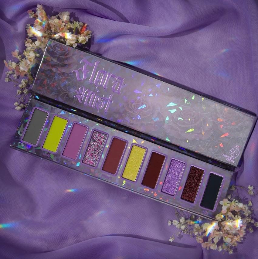 Flora Mist palette open on lilac satin with dried flowers, catching rainbow light on its holographic lid